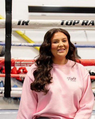 Eve Lister sitting on the edge of a boxing ring in a Fight Like a Girl sweatshirt