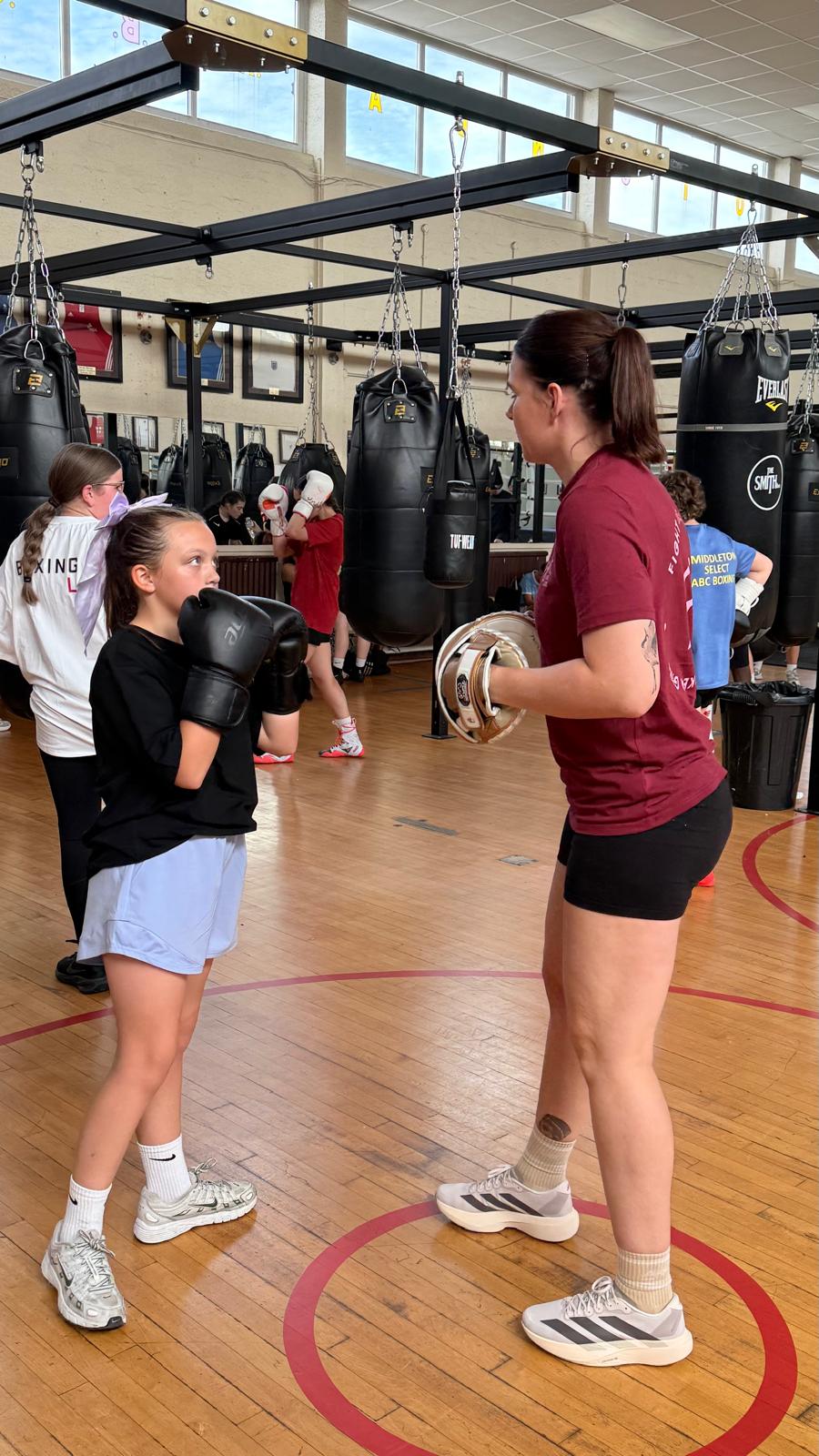 A girl with her guard up facing a coach holding pads